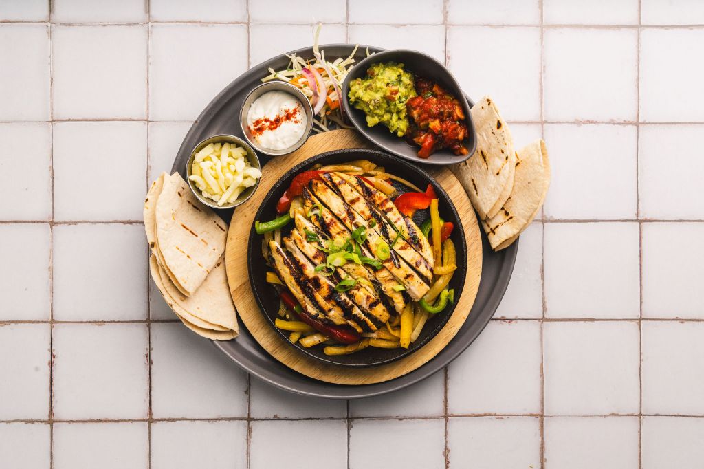 Las Iguanas fajitas. Grilled chicken with peppers and onions surrounded by folded wraps, vibrant dips and garnish.