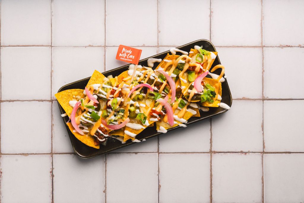 A rectangular plate piled with nachos, a little flag saying 'prepared with care. The tortilla chips are covered in vibrant ingredients. 